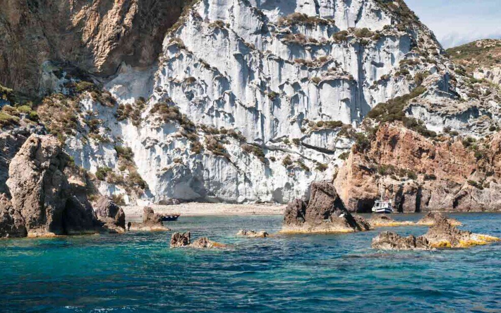 Calacaparra vista dal mare con le sue rocce bianche che scendono a strapiombo su una piccola spiaggia circondata da piccoli scogli affioranti.