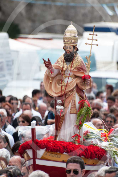Statua di San Silverio in primo piano su una barca portata a braccia dai fedeli in processione.