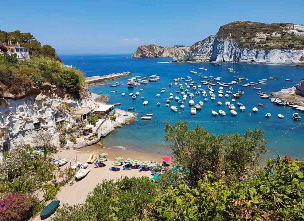 Una piccola spiaggetta con tante barche in mare di fronte chiamata pisscine naturali