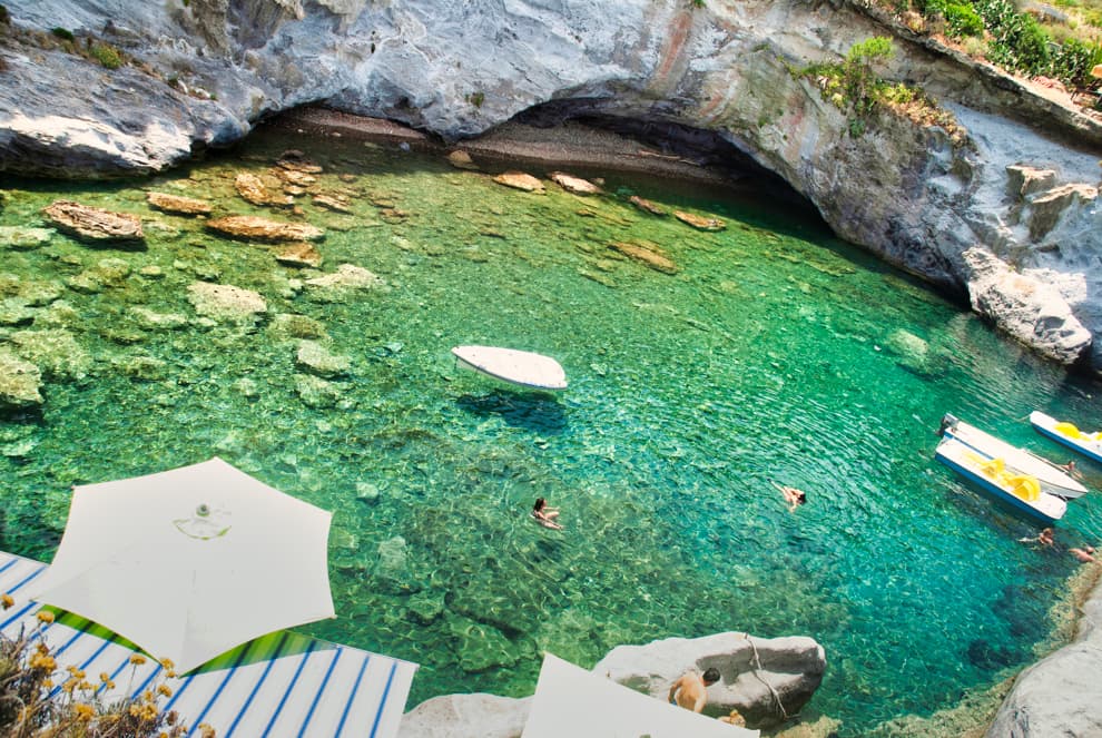 Ponza-piscina-naturale Una vasca naturale circondata dalla roccia a forma di un cerchio piena d'acqua di mare con barchette che galleggiano e la gente si fa il bagno.