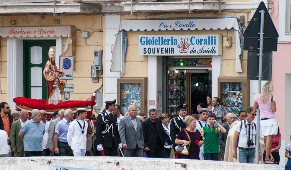Gente che accompagna la statua di San Silverio su una barca colma di fiori rossi alla festa del santo.
