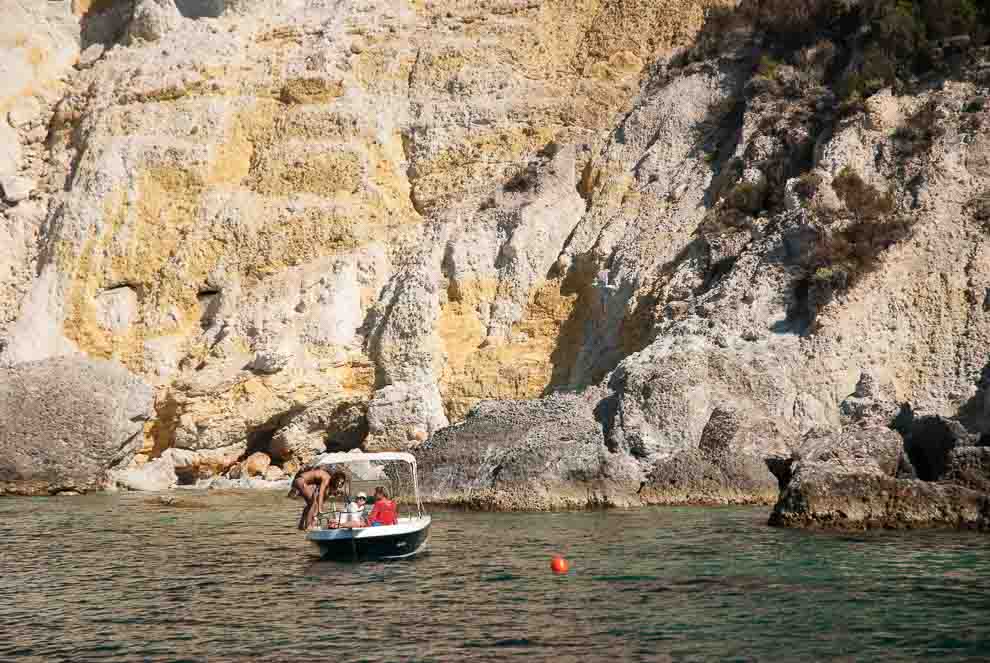 Ponza, Punta incenso Una roccia a picco sul mare colore giallo limone con davanti alla costa una barca ormeggiata con delle persone.