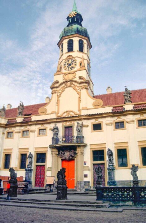 Facciata della chiesa di Loreto di Praga con il suo campanile con orologio dorato e nicchie e statue di santi.