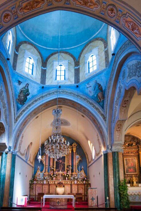 L'interno della Cattedrale cattolica di San Giovanni Battista semplice, con begli affreschi, un grande lampadario che pende dal soffitto a volta e vetrate sotto la cupola.