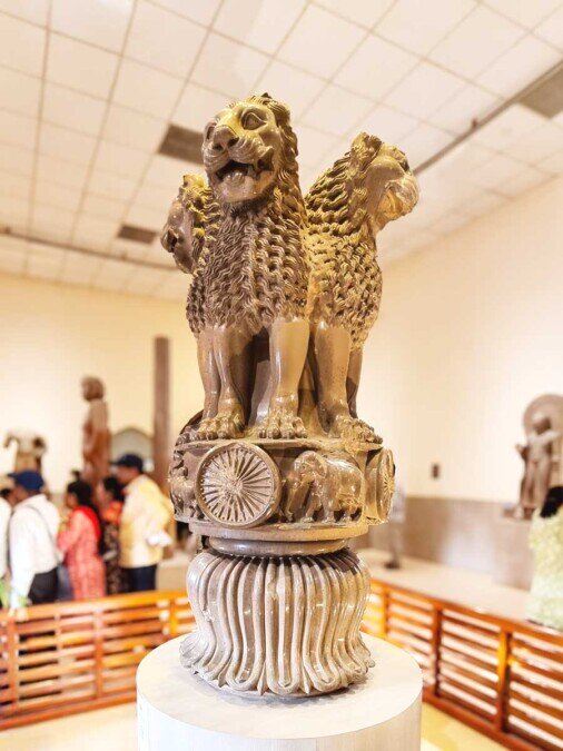 Scultura con i quattro leoni di Ashoka Nel museo di Sarnath una colonna con in cima quattro leoni in piedi disposti di schiena fra loro, con sotto un ripiano a forma di ruota con ai bordi alcune sculture di animali, e sotto ancora un vaso a forma di campana.