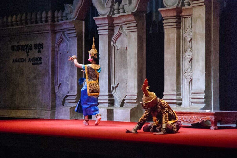 La ragazza col costume da Apsara lotta e vince il demone che rimane in ginocchio e con la testa bassa da sconfitto.