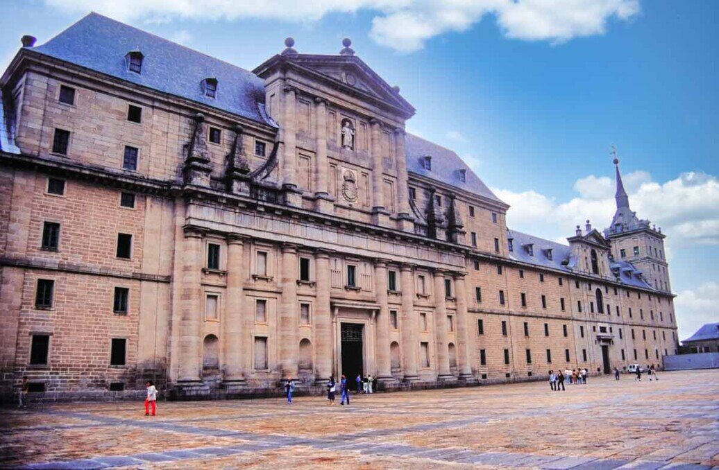 Facciata monumentale del monastero di San Lorenzo de El Escorial, con la lunga struttura in pietra grigia, finestre regolari e torri angolari, sotto un cielo nuvoloso.