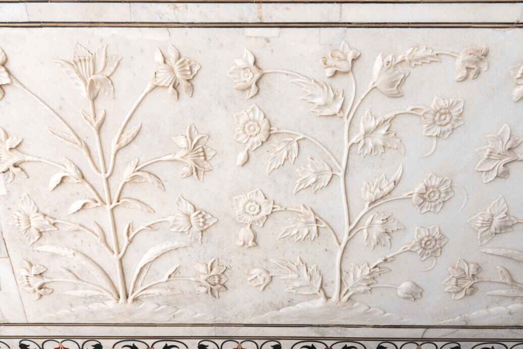 Rappresentazioni realistiche in bassorilievo di fiori in marmo bianco si trovano sulle pareti inferiori della tomba del Taj Mahal, mettendo in risalto la texture del marmo levigato.