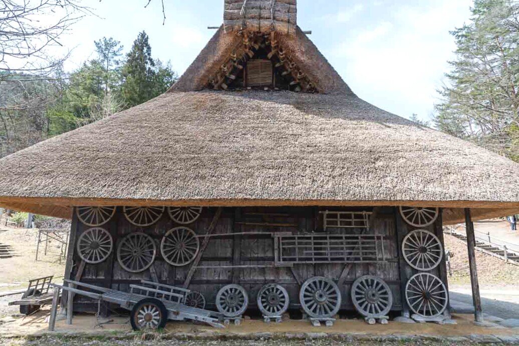 Hida Folk Village deposito per attrerzzi agricoli Edificio in legno con grande tetto spiovente e una parete ricoperta da tante ruote per carretti
