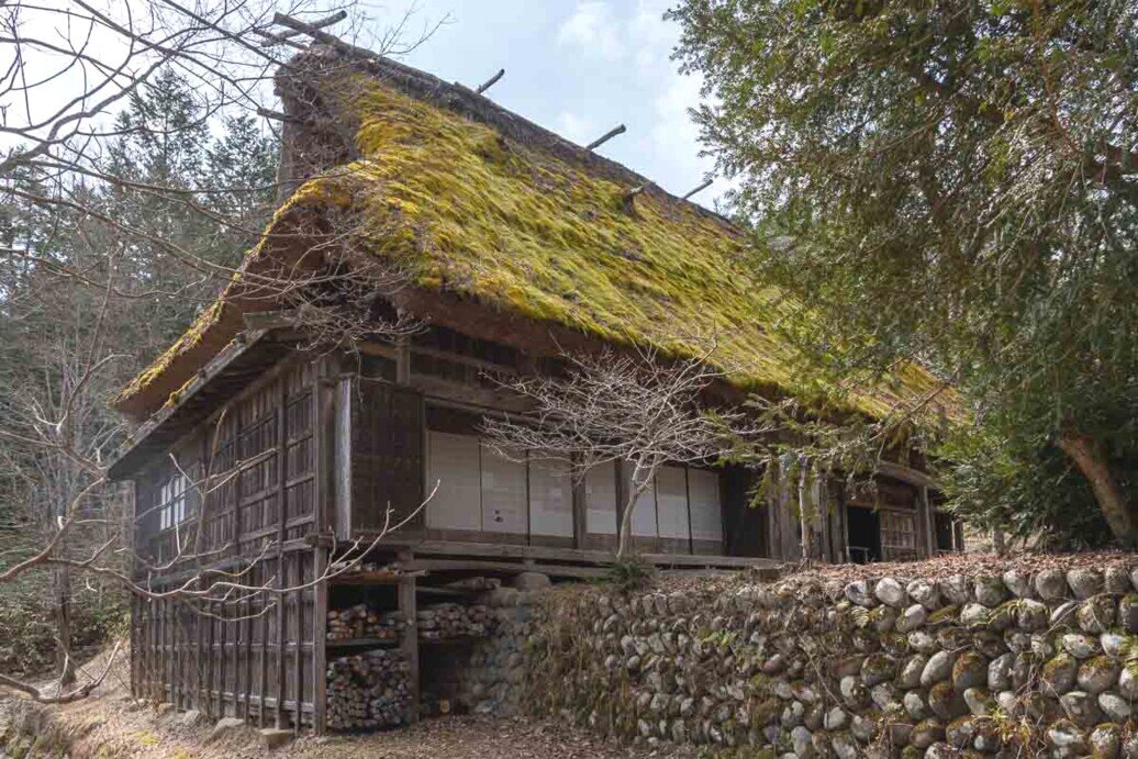 Hida Folk Village tetto spiovente Casa contadina in legno con tetto molto spiovente ricoperto di vegetazione e circondata da un muretto in pietre