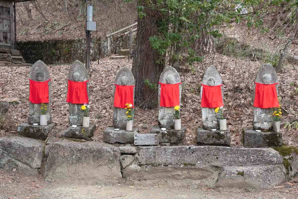 Hida Folk Village statue di jizo Sei piccole statuine di jizo una a fianco all'altra posizionate all'aperto e ciascuno con un bavaglino rosso.