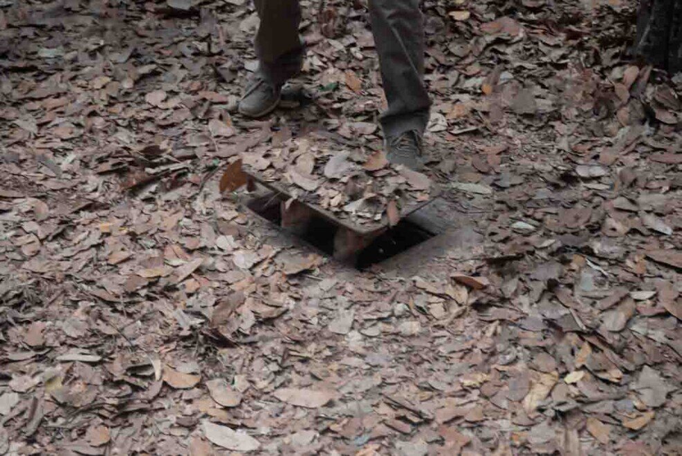 Un uomo solleva un coperchio ricoperto di fogliame che nascondeva una delle aperture di accesso al tunnel vietnamita che serviva per evitare i bombardamenti degli americani.
