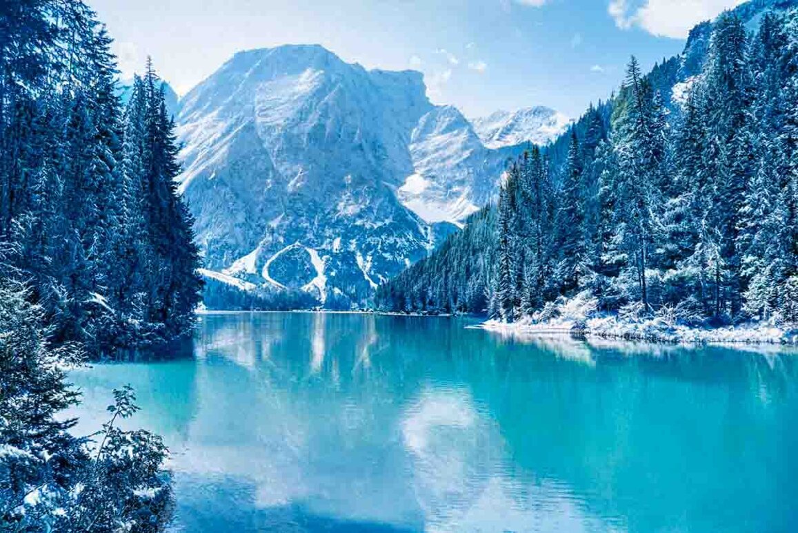 Montagna e alberi innevati che si specchiano sull'antistante lago di Braies.