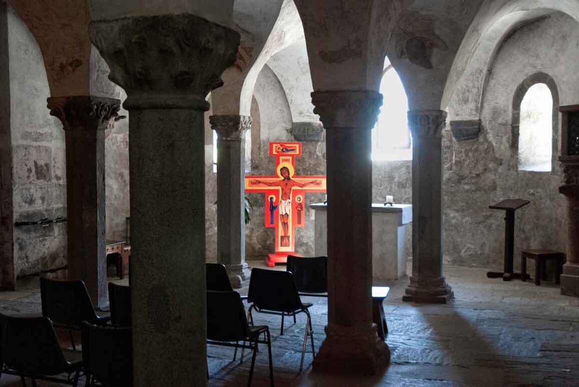 L'interno del Duomo di San Candido all'interno di una cripta con, fra le colonne colonne,  un crocefisso rosso.