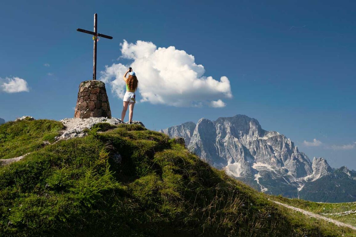 Ragazza intenta a fotografare una grande croce impiantata in cima al Monte Lussari.